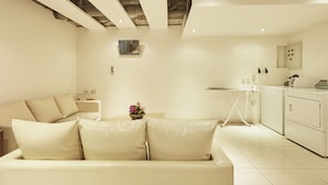 A modern living room with a beige sofa, a small table with a vase of flowers, and a laundry area with a washing machine and dryer. - Taipei Roumei Boutique Hotel (Taipei)