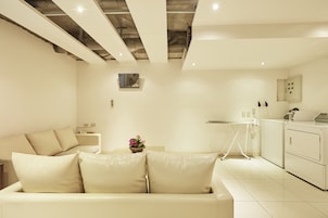 Een moderne woonkamer met een beige bank, een kleine tafel met een bloemenvaas, en een wasruimte met een wasmachine en droger.