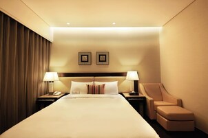 Een hotelkamer met een groot bed, twee bedlampen, een stoel en een nachtkastje met een telefoon.