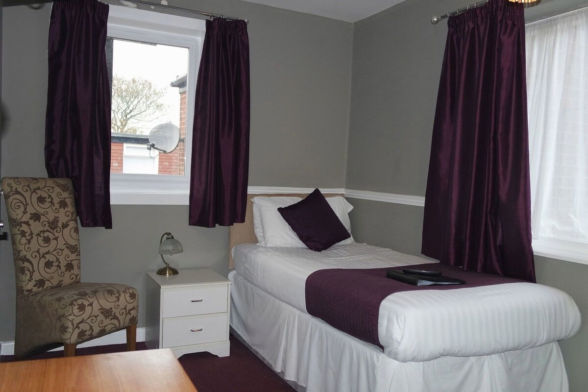 A bedroom with a bed, a chair, a nightstand, and a window with curtains.
