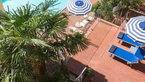 A rooftop pool with blue and white striped umbrellas, sun loungers, and palm trees.