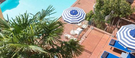 Una piscina en la azotea con sombrillas azul y blanco a rayas, tumbonas y palmeras.