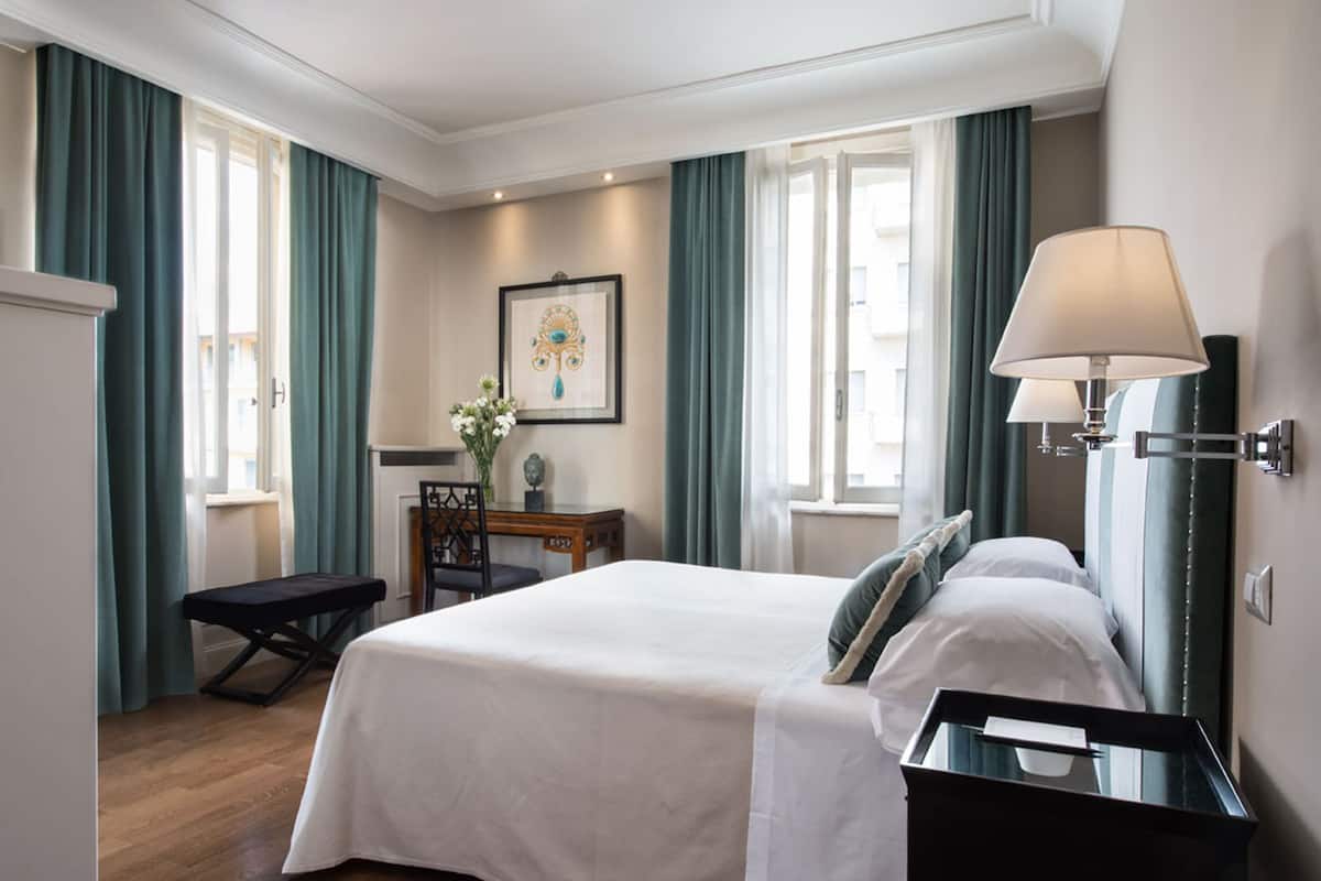 Una habitación de hotel con cama, escritorio, silla, banco y lámpara.