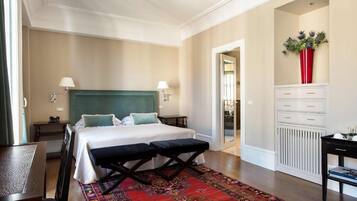 A hotel room with a bed, two bedside tables, a nightstand, a red vase, and a patterned rug.