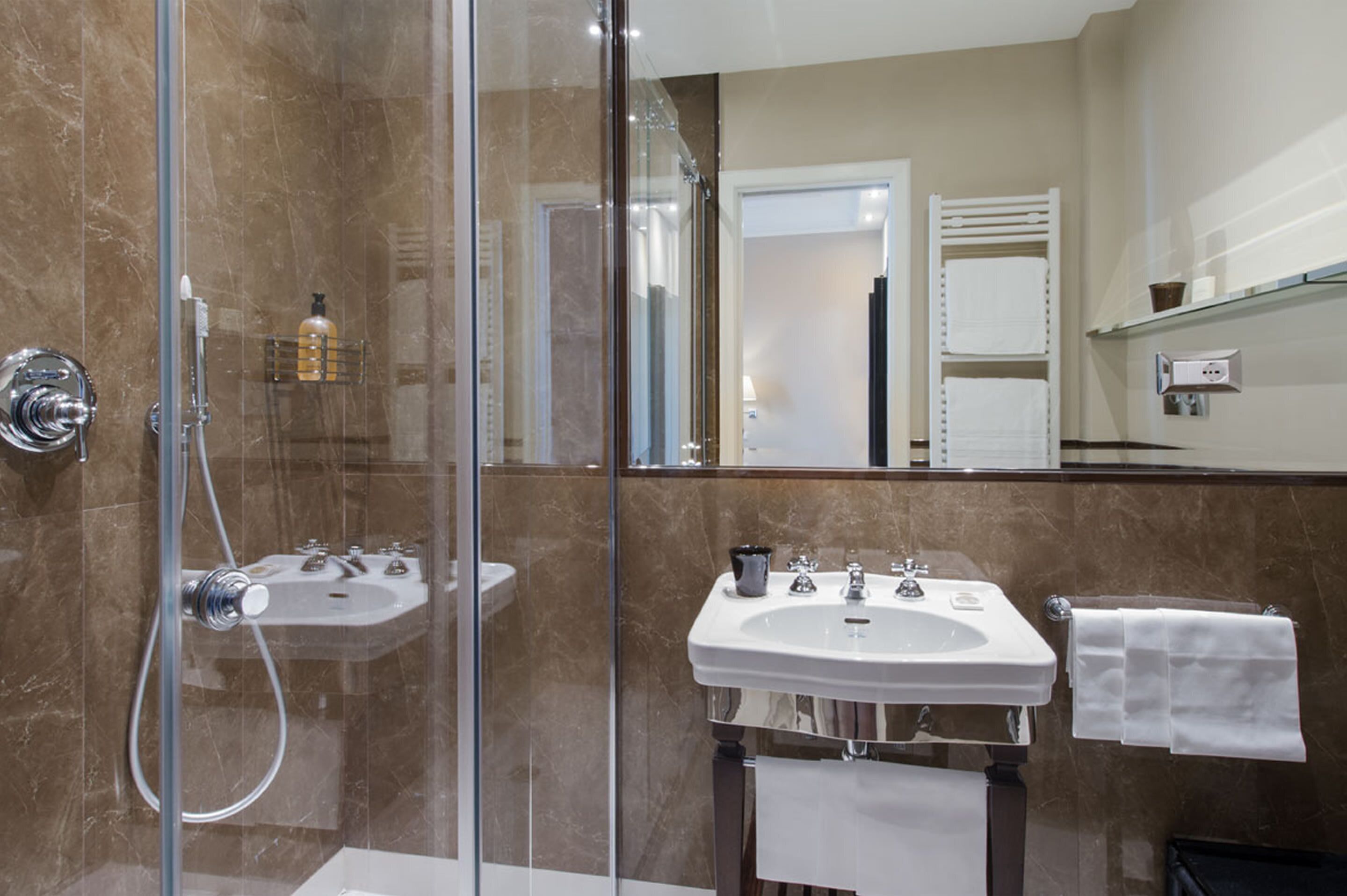 Un baño moderno con ducha de vidrio, un lavabo blanco y un espejo que refleja la habitación.