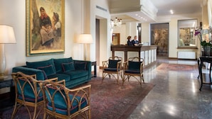 A spacious lobby with a teal sofa, wicker chairs, a large painting, and a reception desk.
