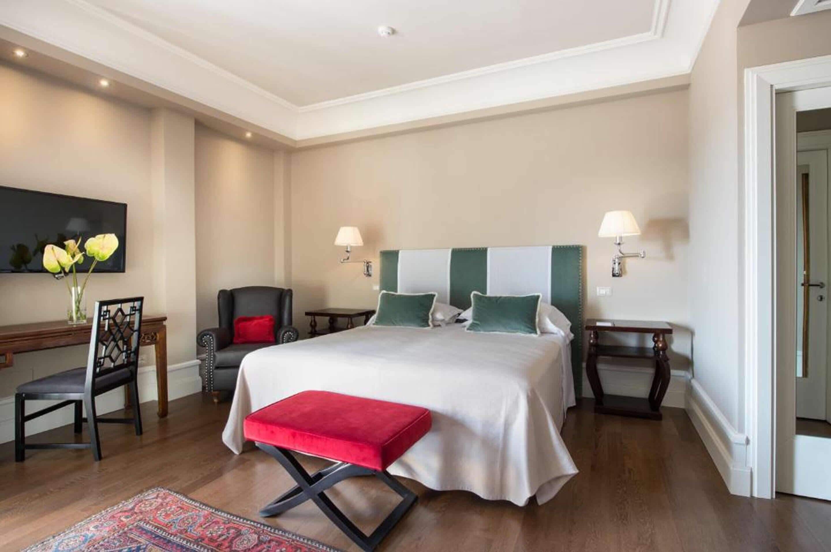 Une chambre spacieuse avec un grand lit, deux tables de chevet, une chaise, un bureau et un téléviseur fixé au mur.