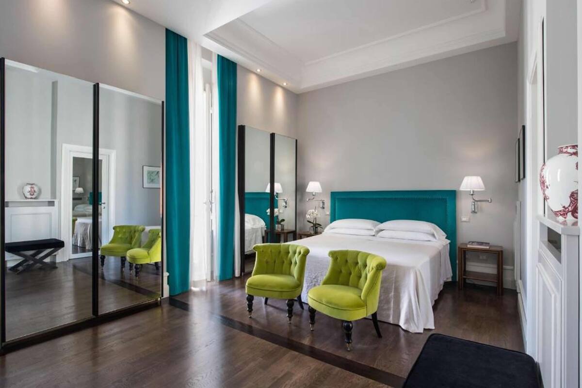 Una habitación de hotel con una cama grande, dos sillas, una mesita de noche y un espejo.