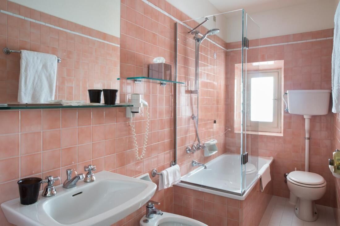 Un baño con dos lavamanos, ducha con mampara de vidrio y un inodoro.