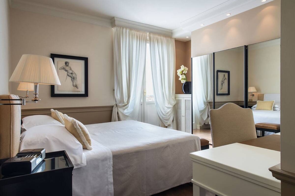 Una habitación de hotel con cama, mesita de noche, lámpara y un espejo grande.