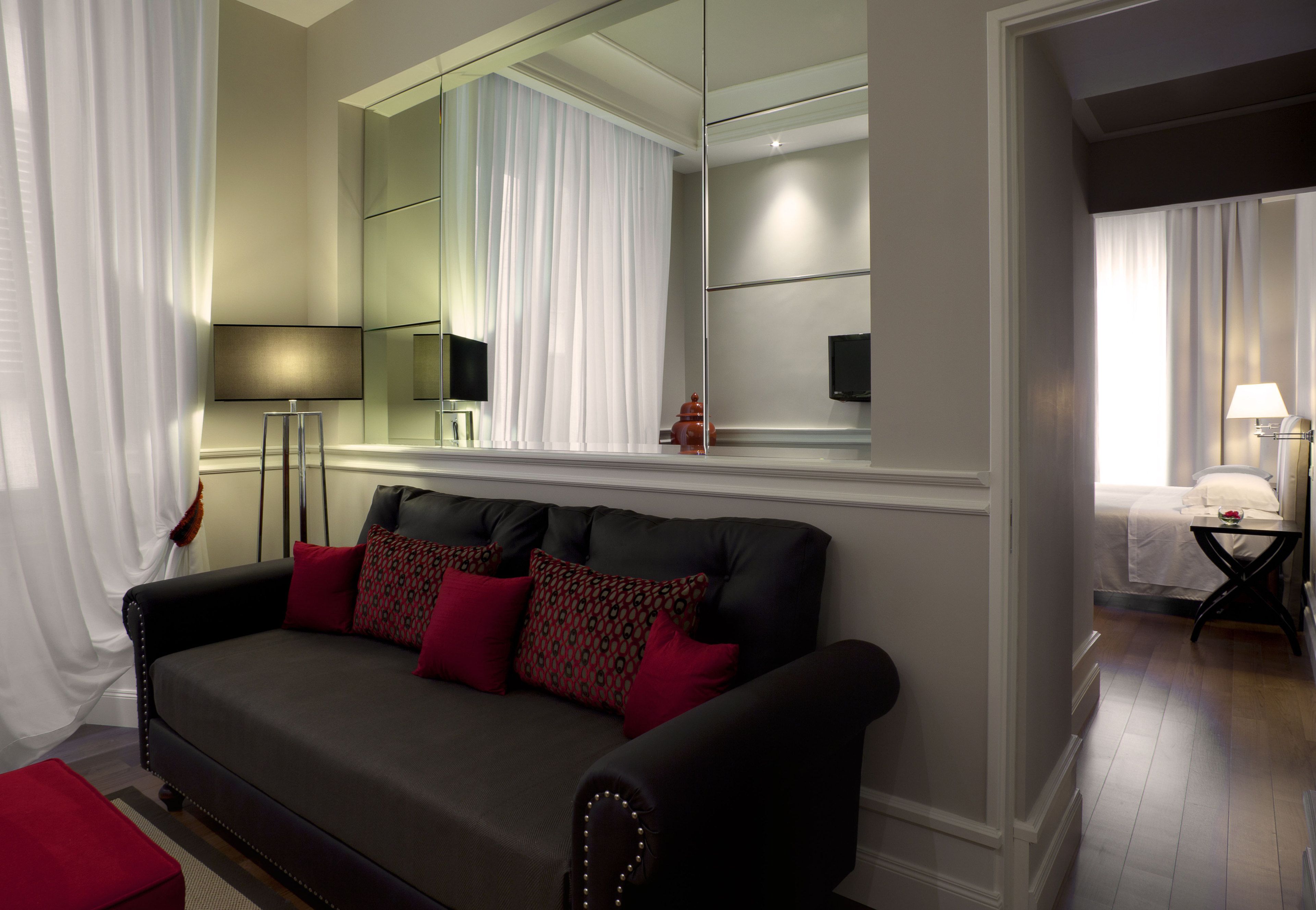 A modern living room with a dark sofa, red cushions, a large mirror, and a flat-screen TV.