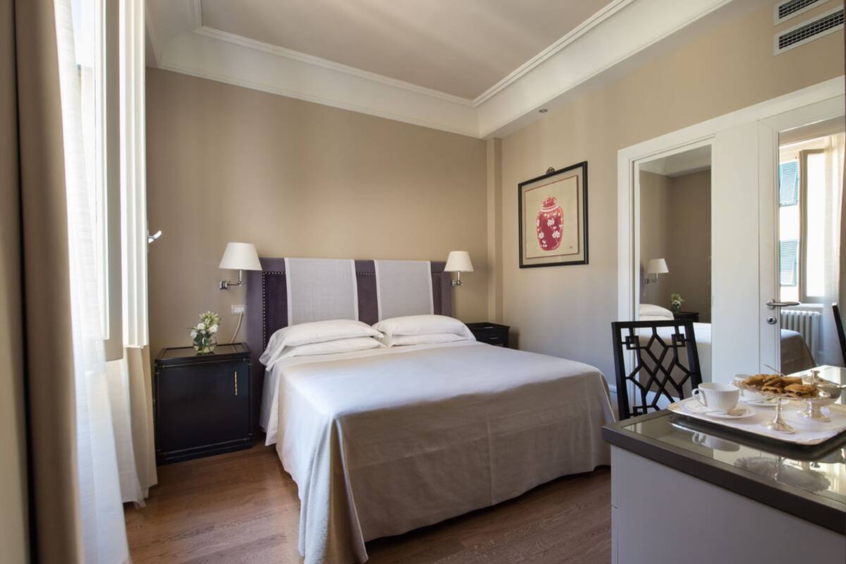 Una habitación de hotel con cama, mesitas de noche, escritorio con silla y espejo.