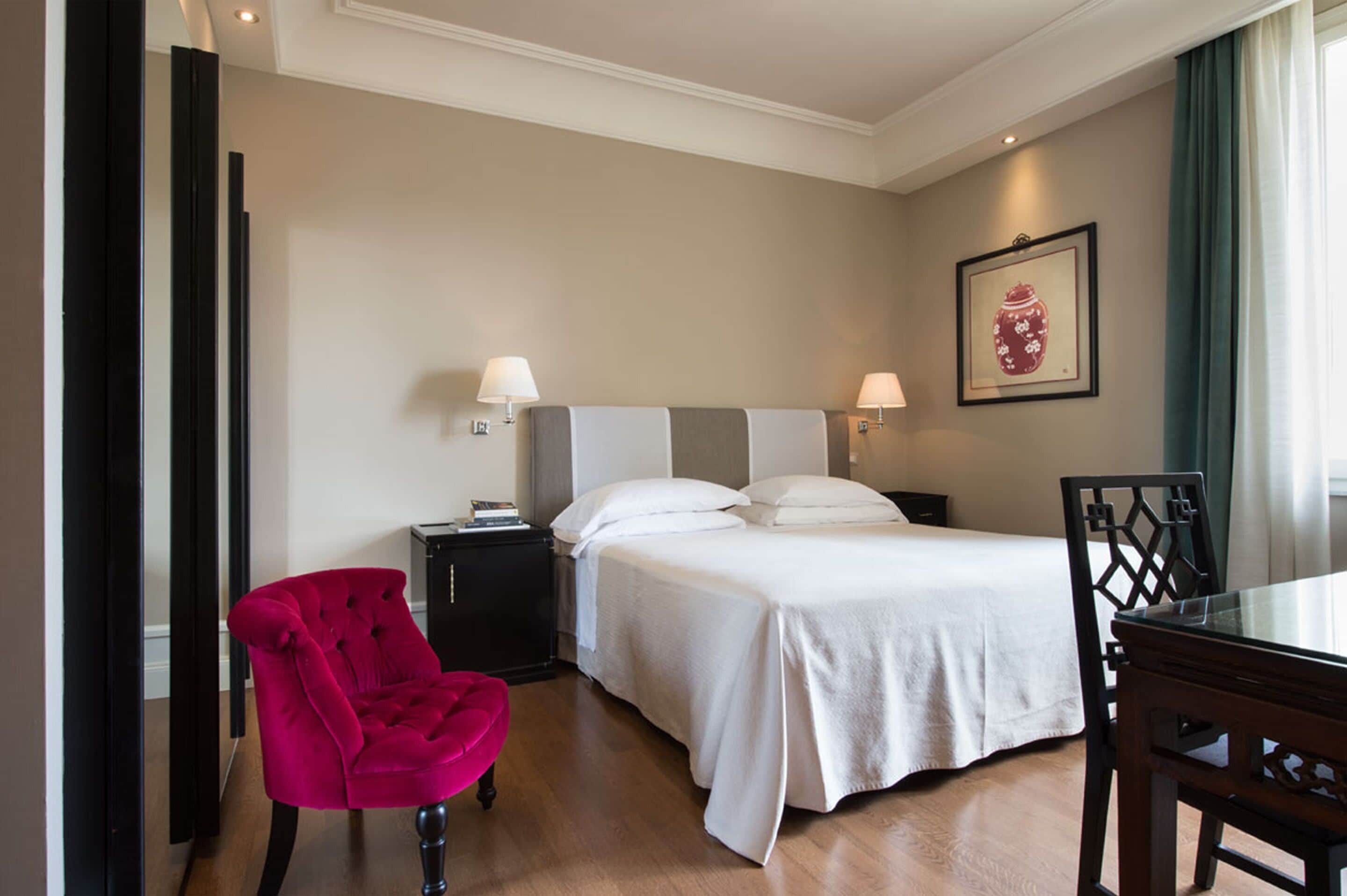 A hotel room with a bed, bedside tables, a chair, and a dining table.