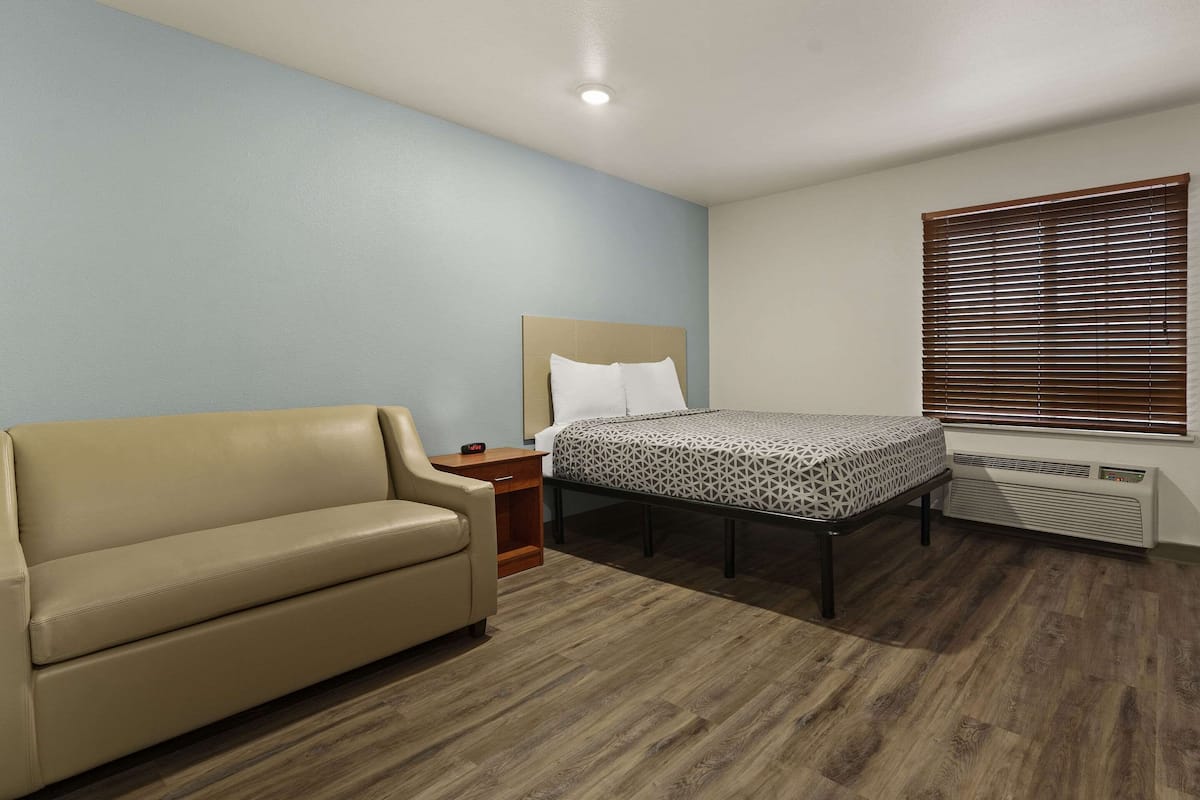 A bedroom with a bed, a sofa, a nightstand, and a window with blinds.