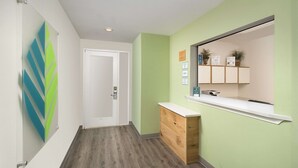 A hallway with a wooden cabinet, a white door, and a green wall with a mirror and small potted plants.