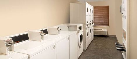 A laundry facility with multiple washing machines and dryers, a ventilation system, and a wall-mounted beverage dispenser.