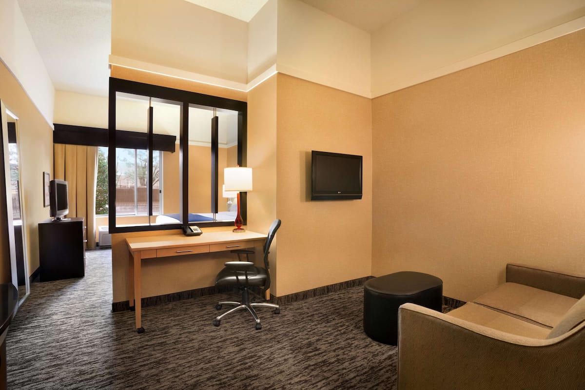 Habitación de hotel con escritorio, silla, televisor y un pequeño sofá.