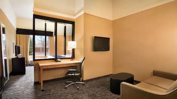 A hotel room with a desk, chair, TV, and a small sofa.