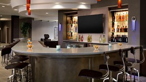 A modern bar area with a curved counter, multiple stools, and a variety of bottles on shelves.