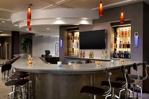 A modern bar area with a curved counter, multiple stools, and a variety of bottles on shelves.