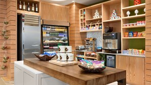 A modern kitchen with wooden cabinets, a stainless steel refrigerator, and a variety of food items and beverages on shelves.