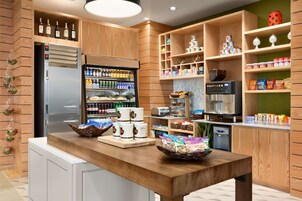 A modern kitchen with wooden cabinets, a stainless steel refrigerator, and a variety of food items and beverages on shelves.