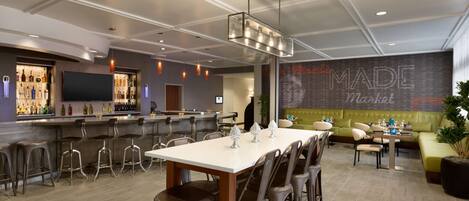 A modern bar area with a long counter, stools, and a large screen.