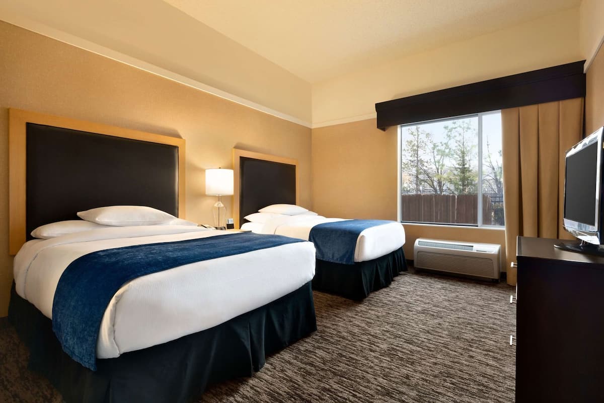 Habitación de hotel con dos camas, televisión, ventana con cortinas y aire acondicionado.