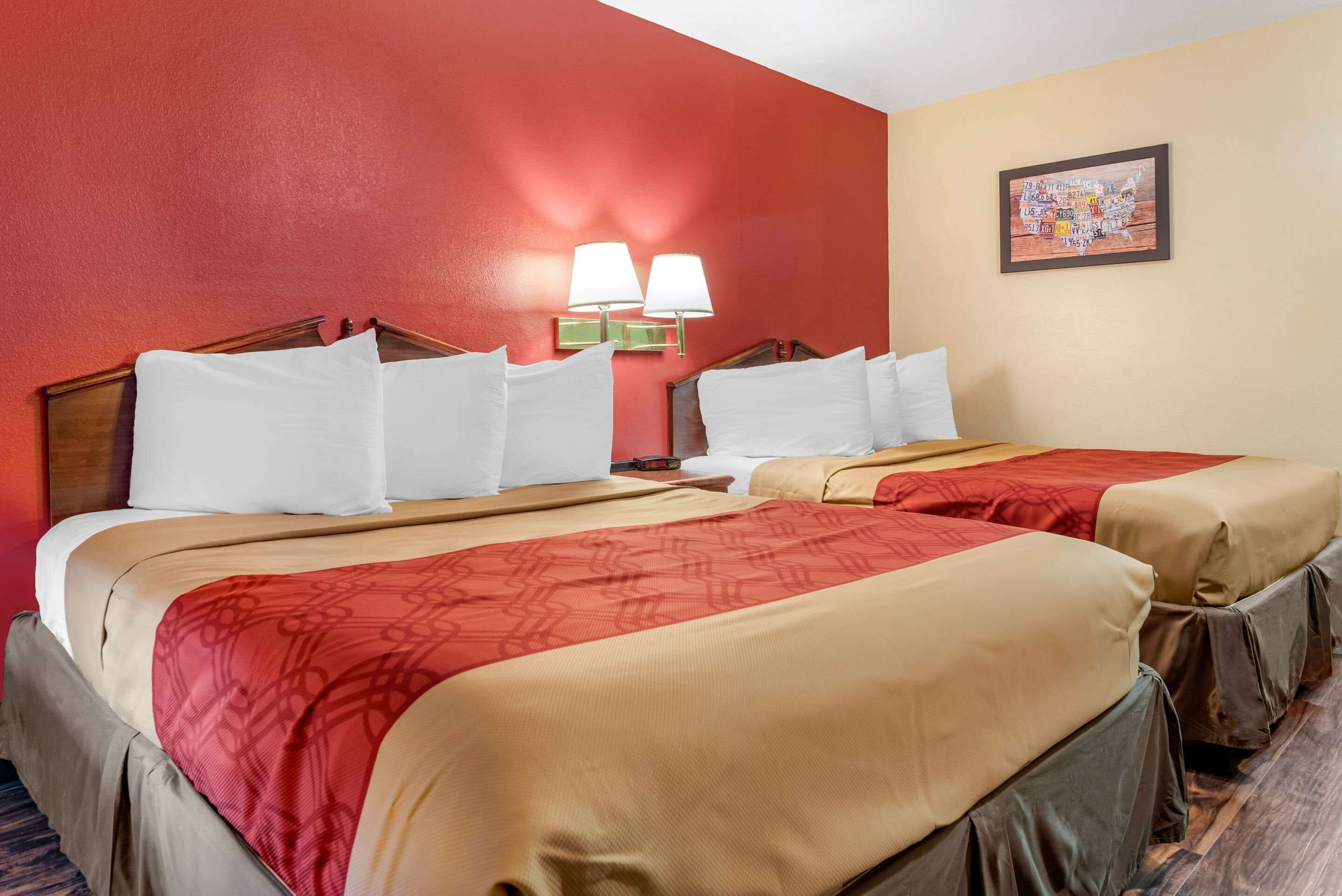 A hotel room with two beds, red walls, and a framed map on the wall.