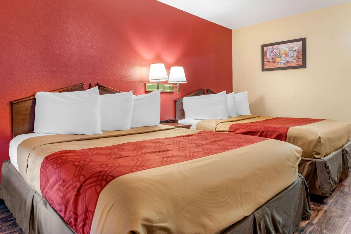 A hotel room with two beds, red walls, beige bedding, and a framed map on the wall.