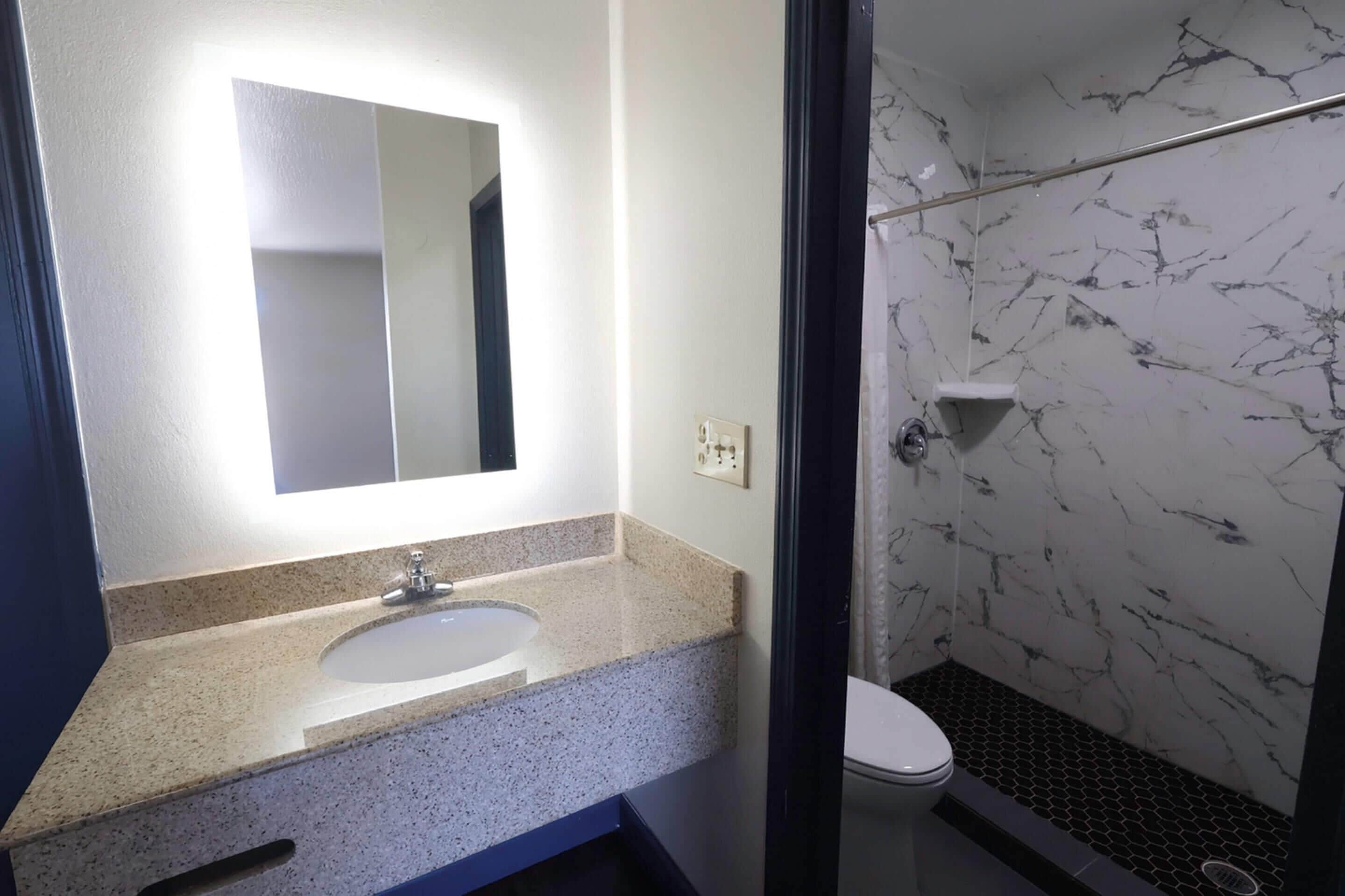 A bathroom with a marble shower, a sink with a mirror, and a toilet.