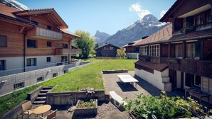 Un pati amb edificis de fusta, un jardí petit i una vista a la muntanya.
