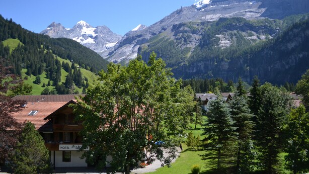 Hotel amb vista a la muntanya, envoltat de verdor exuberant i pics nevats.