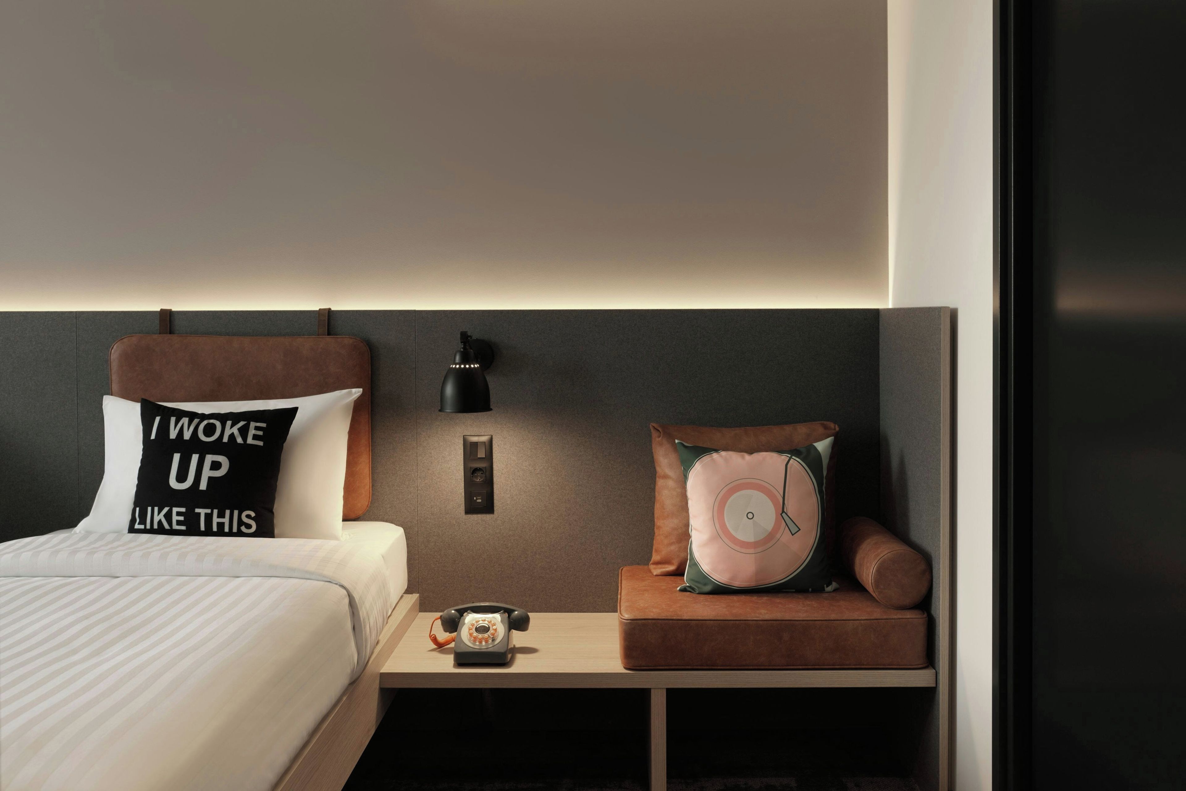 A modern bedroom with a bed, bedside table, and a nightstand with a telephone.