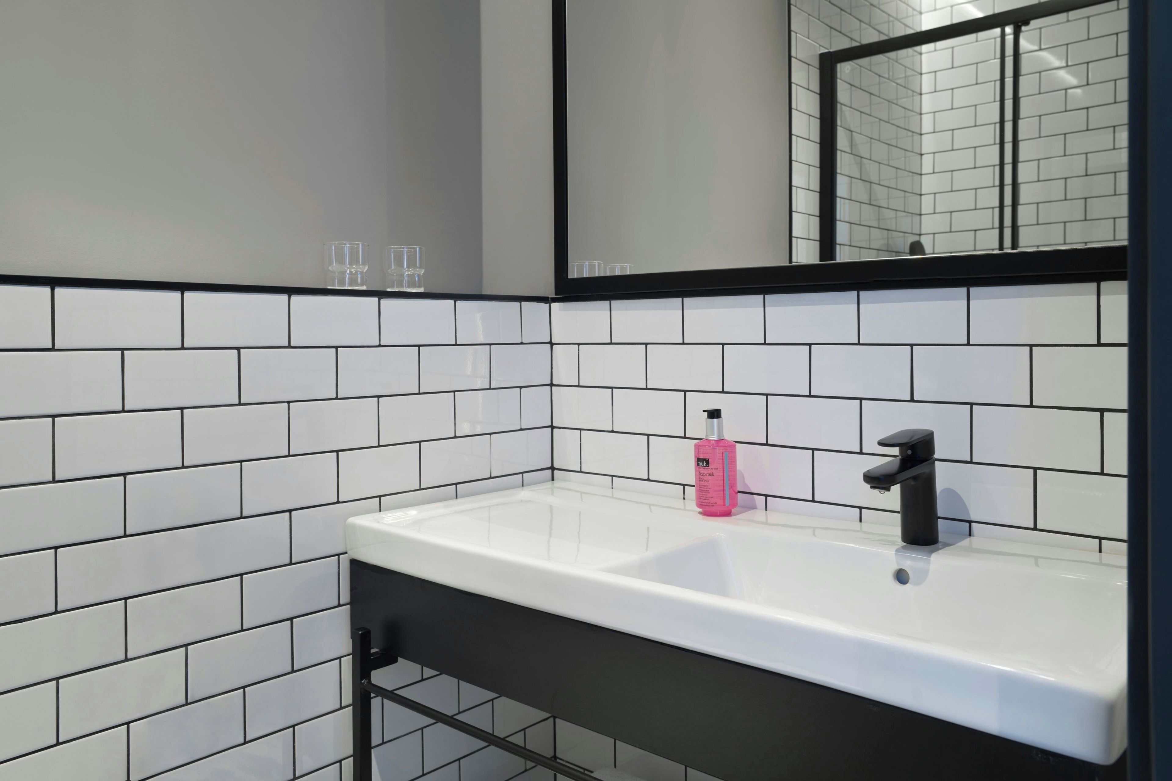 A bathroom with white subway tiles, a black-framed mirror, a white sink, and a black faucet.