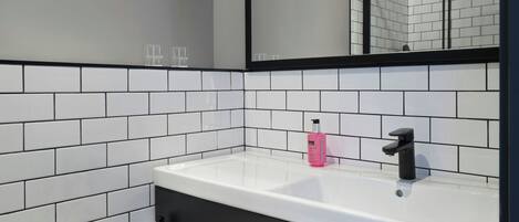 A bathroom with white subway tiles, a black-framed mirror, a white sink, and a black faucet.