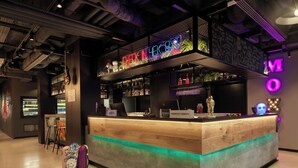 A modern bar area with neon signage, a wooden counter, and a seating area with a skateboard. - Moxy Belgrade (Belgrade)