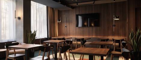A modern restaurant with wooden tables and chairs, large windows, and a flat-screen TV on the wall.