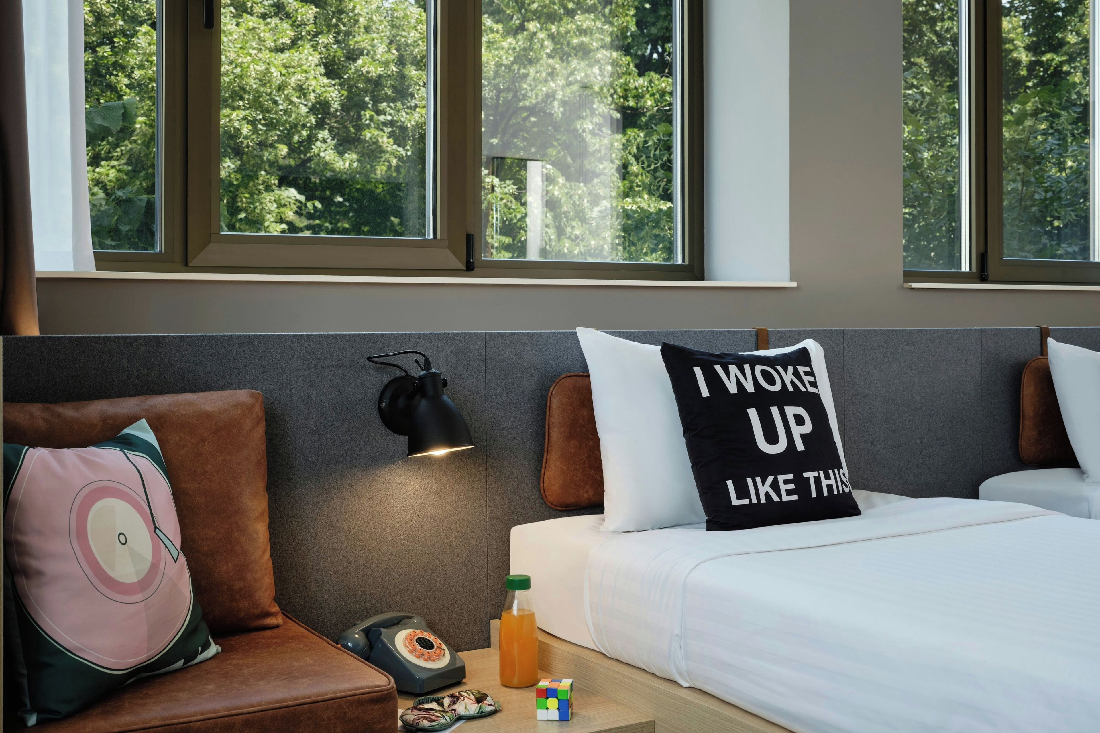 A hotel room with a bed, a nightstand, a lamp, and a window with a view of trees.