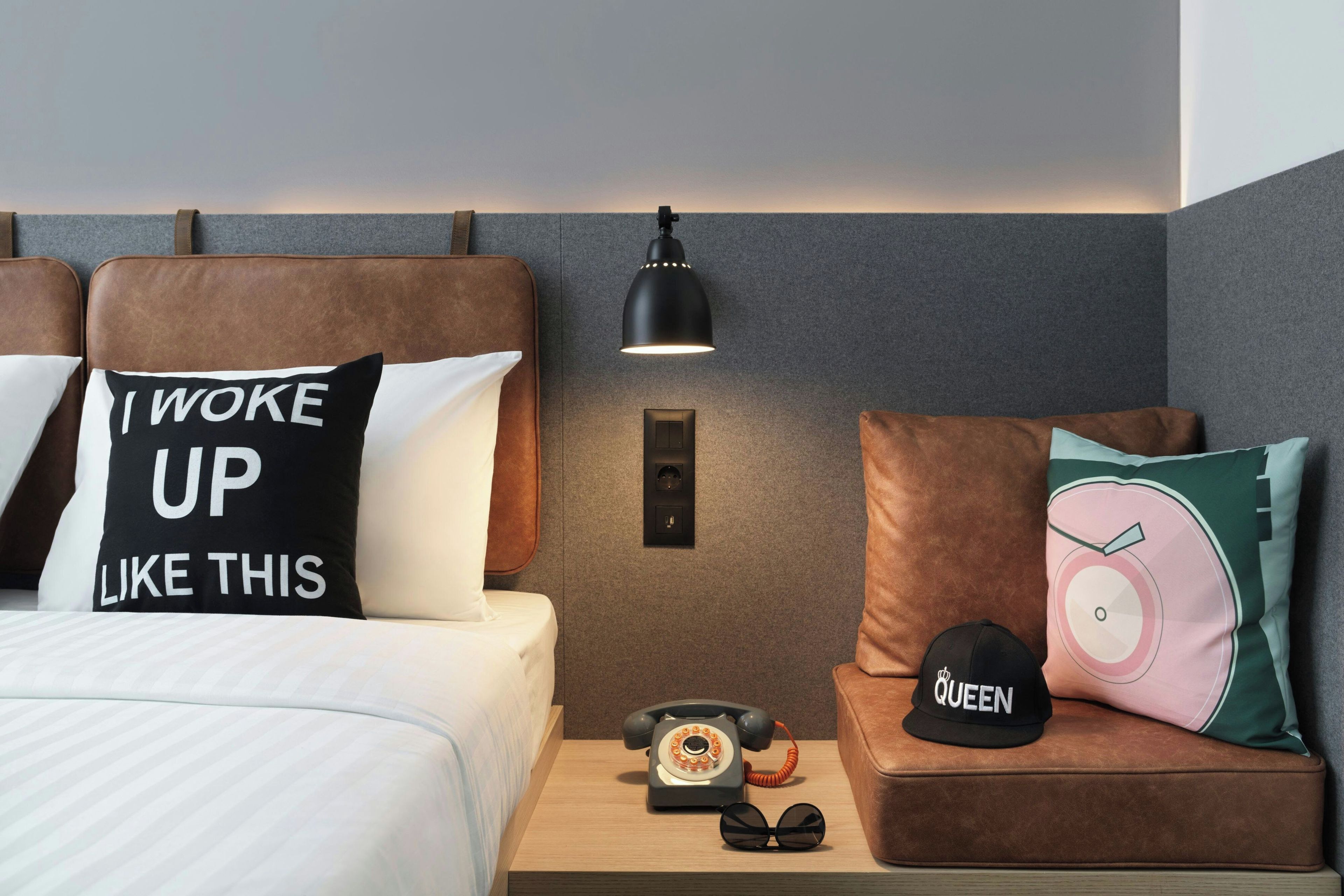 A hotel room with a bed, a nightstand, a lamp, a telephone, and a cap.