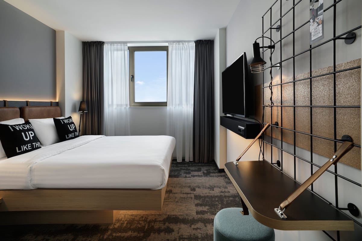 A hotel room with a bed, a desk, a TV, and a window with curtains.