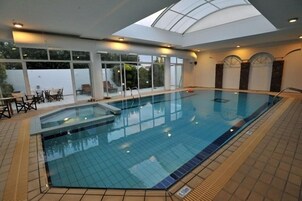 En inomhuspool med ett glastak, kaklat golv och en liten pool i anslutning till den.