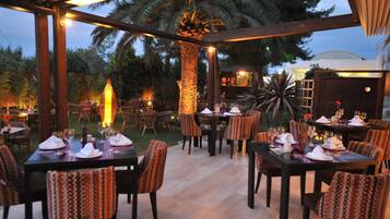 Un área de comedor al aire libre con mesas dispuestas para dos, rodeada de sillas con tapicería estampada.