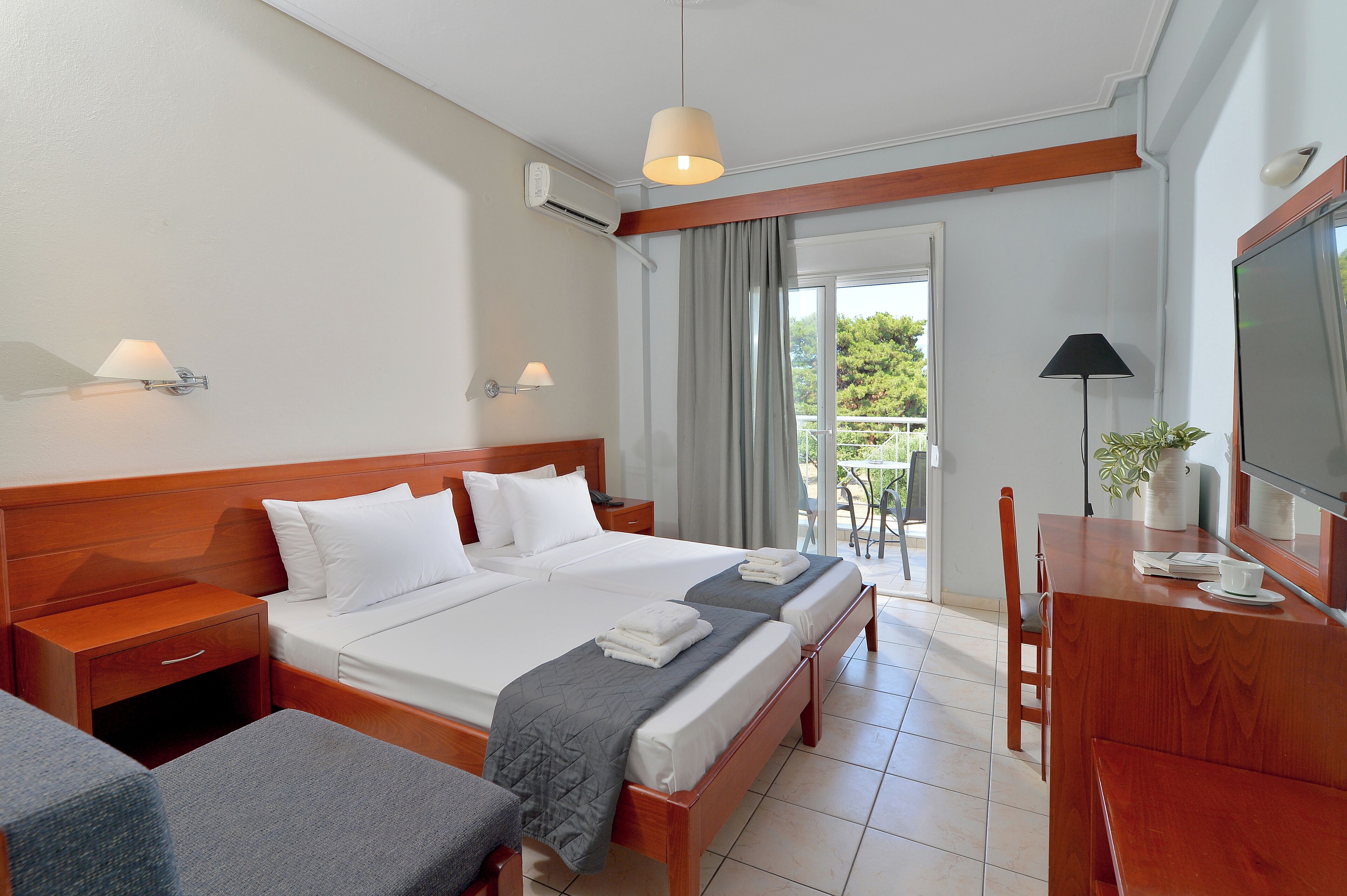 Habitación de hotel con una cama grande, un escritorio, una silla y un balcón con vistas a la vegetación.