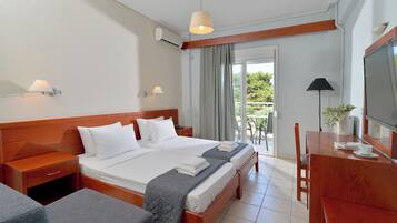 Habitación de hotel con una cama grande, un escritorio, una silla y un balcón con vistas a la vegetación.