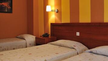 A hotel room with two beds, a nightstand, a lamp, and a fruit basket on the bed.