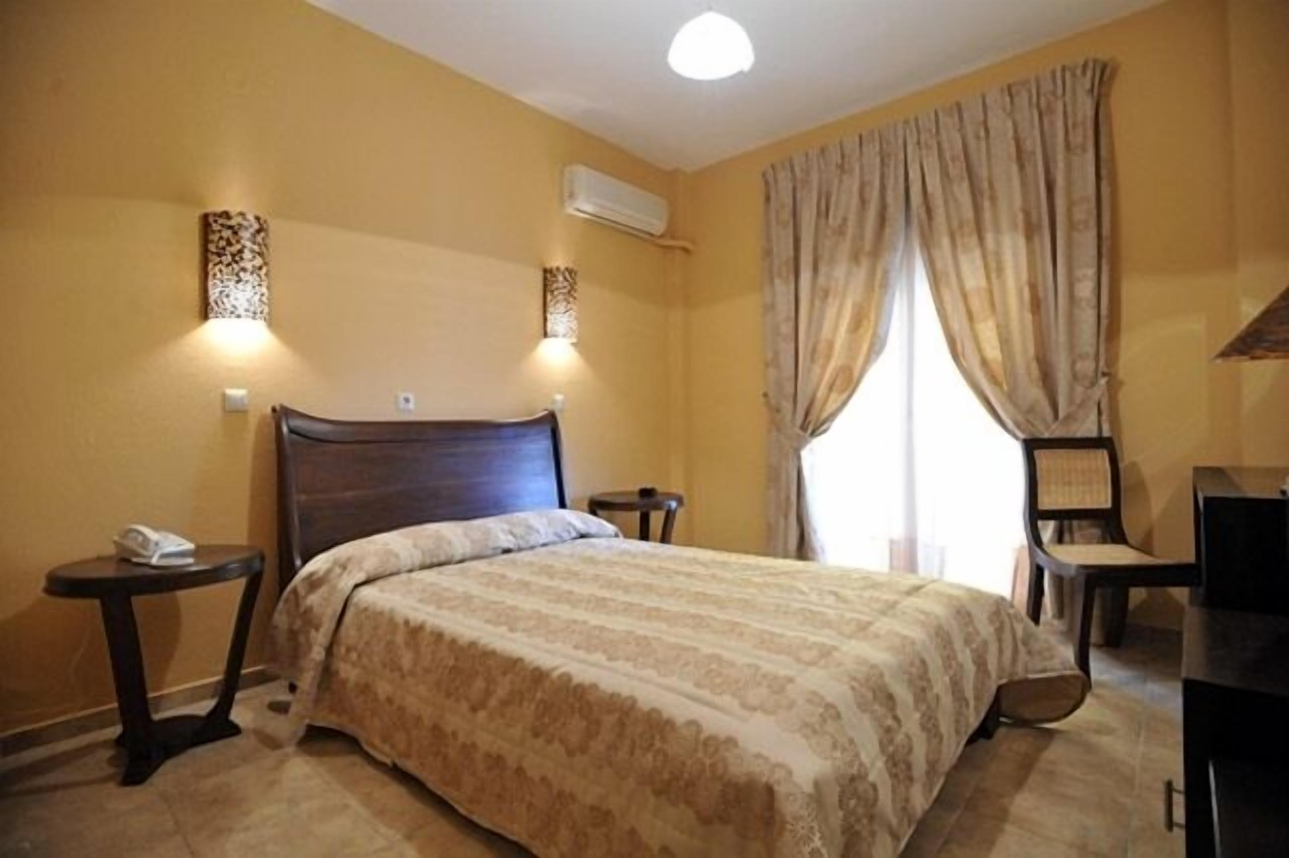 A hotel room with a large bed, a desk, a chair, and a small table with a phone.