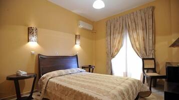 A hotel room with a large bed, a desk, a chair, and a small table with a phone.