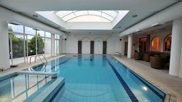 Una piscina interior con tragaluces, paredes de vidrio transparente y un área de descanso con asientos.