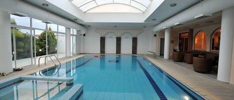 Una piscina interior con tragaluces, paredes de vidrio transparente y un área de descanso con asientos.